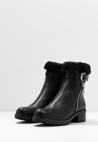 Bottes basses en cuir noir avec un manchon en fausse fourrure, une fermeture éclair latérale et un talon bloc. Dotées d'une semelle texturée pour une meilleure adhérence.