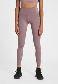Licht mauve hoge taille leggings van rekbaar materiaal, met een subtiele merklogo in het wit nabij de linkse heup. Glad textuur.