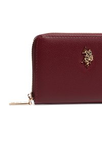 Burgundská kožená peněženka s texturovaným povrchem, zlatými doplňky a emblémem s pólistou. Zipové uzavírání podél horního okraje.