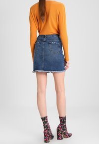 Denim minirok met een rafelige zoom, gecombineerd met een geribde oranje trui. Enkellaarsjes met bloemenprint maken de outfit compleet.