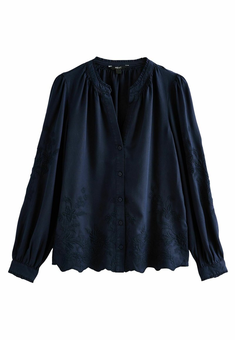 Blusa blu navy con maniche lunghe, chiusura a bottoni, scollatura arricciata e motivi floreali in rilievo lungo l'orlo e le maniche. Tessuto morbido.