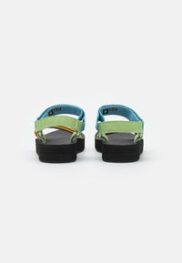 Sandaler med remmer i teal, grønt og gult tekstil, en teksturert svart såle og et enkelt bakre remdesigne.