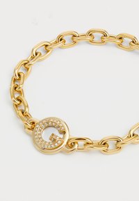 Pulsera de cadena de oro con eslabones ovalados, un cierre redondo adornado con strass y un acento estilizado de la letra G.