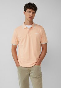 Brzoskwiniowa koszulka polo z kontrastowym jasnoniebieskim kołnierzykiem i akcentami na rękawach, z małym logo na lewej części klatki piersiowej i strukturalną tkaniną.