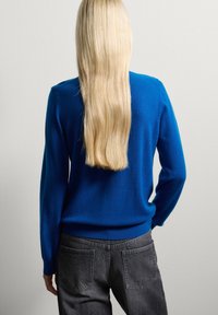 Suéter azul de manga larga, textura suave, escote redondo, combinado con jeans de mezclilla gris, con bolsillos traseros y un corte holgado.