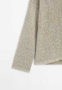 Light gray knitted sweater detail showing a loose weave, long sleeve, and a relaxed fit with a slightly curved hem.