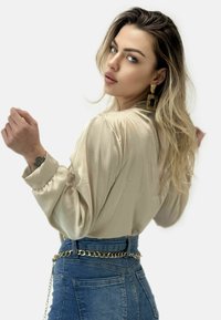 Lys beige satinbluse med puffede ærmer, båret med højtaljede blå denimjeans. Bemærkelsesværdig guld kæde bæltedetalje.