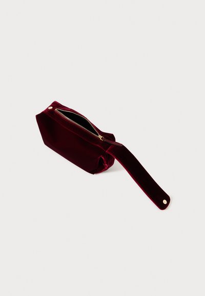 Burgundy velour kosmetikpose med en guld lynlås, rektangulær form og et vedhæftet bånd til nem bæring. Tekstureret og blød overflade.