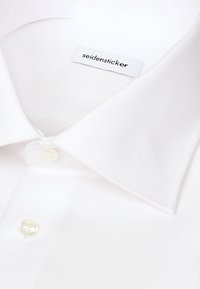 Col de chemise blanche et boutons avec une étiquette visible portant la mention "seidensticker" à l'intérieur de l'encolure.