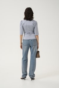 Blusa azzurro chiaro, strutturata, con maniche a sbuffo, abbinata a jeans larghi azzurro chiaro. La modella tiene in mano una piccola borsa con stampa leopardata.