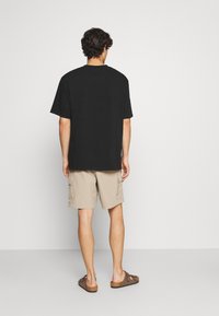 Sort bomulds t-shirt med korte ærmer, beige cargo-shorts og brune sandaler; simpel, afslappet pasform, minimalistisk design uden grafik.