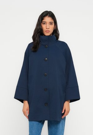 Tmavomodrý kabát s vysokým golierom, zvonovými rukávmi a zapínaním na gombíky vpredu. Má dve bočné vrecká a hladkú, textúrovanú látku.