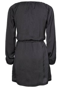 Svart klänning med prickar, lång ärm, elastisk midja och samlad ryggdesign. Tillverkad av lätt tyg med små vita prickar.