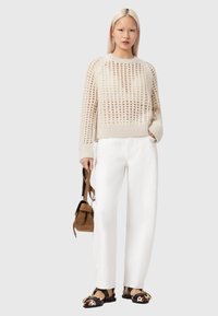 Pull beige en maille avec motif ajouré, ourlet côtelé, associé à un pantalon blanc à jambes larges et des chaussures plates noires avec des accents imprimé vache.