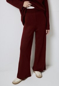 Maroon wide-leg knit pants with a smooth texture and elastic waistband, paired with white and beige sneakers. Simple and functional design.