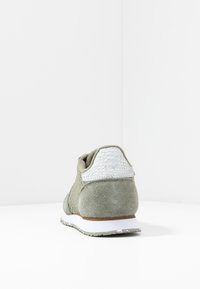 Grüner Wildledersneaker mit strukturiertem grauen Überzug an der Ferse, weißer Sohle und hellgrauen Akzenten. Verfügt über einen gemusterten hinteren Abschnitt.