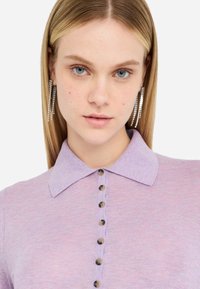 Top lavorato a maglia lilla con design colletto, caratterizzato da una patta con bottoni e tessuto testurizzato. Nota per la sua colorazione morbida e il motivo sottile.