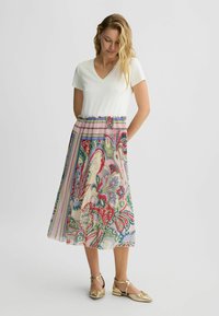 Haut blanc à col en V avec des manches courtes assorti à une jupe midi plissée ornée d'un motif floral et géométrique coloré, complétée par des sandales dorées.