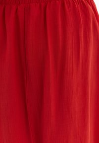 Tessuto leggero e rosso con una morbida texture arricciata. Presenta una vita elastica e una forma fluida, ideale per l'abbigliamento casual.