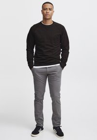 Sweatshirt noir à manches longues, pantalon gris slim-fit et baskets noires avec des rayures blanches. Tissu lisse, design simple, sans motifs notables.