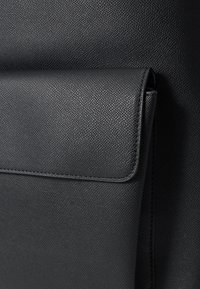 Fekete, texturált bőrtáska fedéllel, sima széllel és finom szemcsemintázattal. Kompakt kialakítás, amely mindennapi használatra alkalmas.