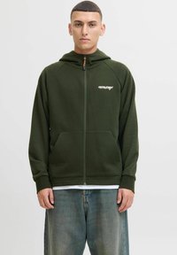 Veste à capuche zippée verte avec un design texturé et des poches kangourou. Elle présente un logo brodé sur la poitrine et une capuche avec cordon de serrage.