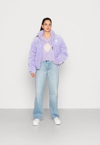 Jakna sa pufastim materijalom u svijetloj lavandi s teksturiranim prugama, uparena s pastelnim argyle džemperom, širokim trapericama i bijelim tenisicama.