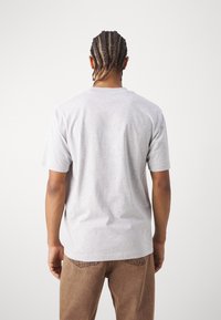 T-shirt gris à manches courtes avec un design classique à col rond, fabriqué en coton doux, associé à un pantalon marron, vu de l'arrière.