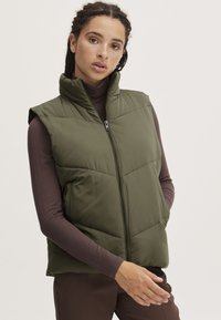 Gilet rembourré vert avec un col montant, fermeture éclair et design sans manches. Présente une texture matelassée et une finition extérieure lisse.