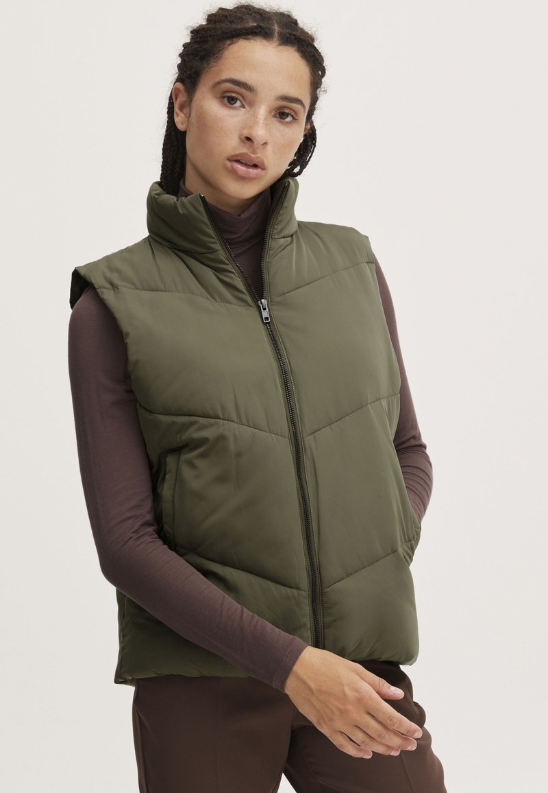 Gilet rembourré vert avec un col montant, fermeture éclair et design sans manches. Présente une texture matelassée et une finition extérieure lisse.
