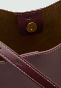 Handtas interieur van leer met een bruine gestructureerde voering, roze bies en een gouden drukknoopsluiting met merkdetail.