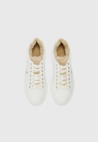 Hvite joggesko med myk beige pelsfôr, øyelet i gullfarge og flate lisser. Glatt materiale med rund tådesign.
