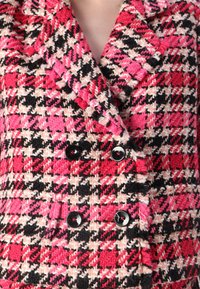 Doppelt geknöpftes Sakko im Hahnentrittmuster mit rosa, schwarz und weißen Farbtönen. Aus strukturiertem Material mit glänzenden schwarzen Knöpfen gefertigt.