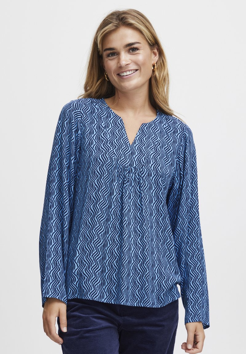 Blue long-sleeve blouse with a wave pattern, featuring a V-neck and gathered detail at the front. Lightweight fabric with a smooth texture.