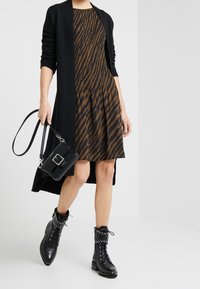 Svart lång cardigan över en brun klänning med vertikala mörka ränder. Stylad med svarta, nithängda ankelstövlar och en liten svart handväska.