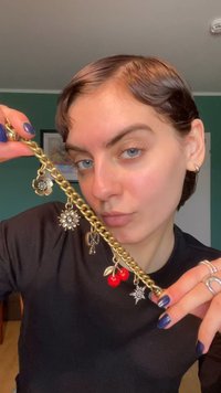 Bracelet en chaîne dorée avec plusieurs breloques : une fleur, une étoile scintillante, une clé et des cerises rouges, présenté sur un fond sombre.