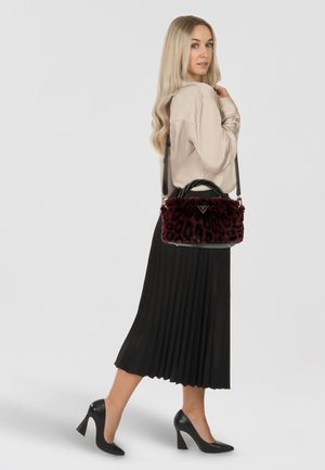 Sac à main en fausse fourrure bordeaux avec un motif léopard, anses en cuir noir, quincaillerie en argent et un design épuré. Jupe plissée noire et talons noirs.