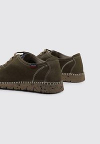 Zapatos de ante verde con costuras beige, punta redonda y suela de goma marrón texturizada. Presentan un diseño casual con un mínimo de detalles.