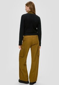 Pull en laine noir avec un col rond associé à un pantalon cargo large couleur moutarde comprenant des poches latérales, une texture lisse et une coupe décontractée.