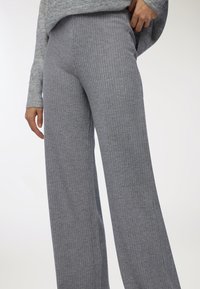 Persona che indossa pantaloni a gamba larga in maglia grigia a coste a vita alta e un top a maniche lunghe abbinato, con una mano appoggiata sui fianchi.