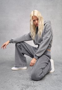 Grijze hoodie en wijde sweatpants gemaakt van zacht materiaal, met geribbelde manchetten en een tailleband met trekkoord. Witte sneakers complementeren de outfit.