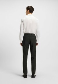 Weißes Langarmhemd mit Knopfdetails und schwarzen gestreiften Hosen, die eine schlanke Passform und glatte Textur aufweisen, von hinten betrachtet.