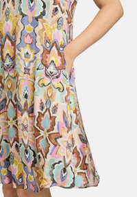 Bunt gemustertes Blumenkleid mit fließendem Design, aus leichtem Stoff gefertigt, mit Taschen und einem Saum, der leicht ausgestellt ist.