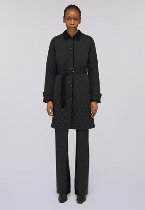 Cappotto nero trapuntato con colletto, chiusura a bottoni e vita con cintura. Presenta maniche lunghe e tasche laterali, abbinato a pantaloni neri e stivali.