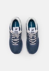 Tummansininen New Balance 574 -lenkkari, joka on valmistettu verkko- ja mokkamateriaalista, vaaleanharmaat nauhat ja valkoiset yksityiskohdat. Sisältää logon kielekkeessä ja sivuilla.