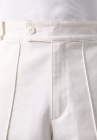 Vita skräddarsydda byxor med en knappstängning, veck och sidofickor. Tyget har en subtil textur och en strukturerad design.