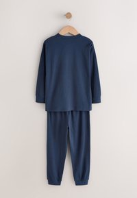 Tamsiai mėlynas dviejų dalių rinkinys, sudarytas iš ilgarankovio viršutinės dalies su apvalia iškirpte ir derančių elastine juosmens ruože kelnių, pagamintų iš minkštos medžiagos.