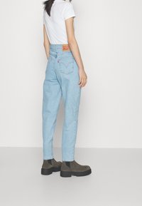 Ljust blå högmidjade jeans med avsmalnande ben, med bakfickor och en brun läderlogga. Kombinerat med mörka ankelskor.