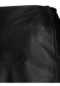 Jupe en cuir noir avec une texture lisse, des coutures angulaires et une fermeture éclair sur le côté. Le design met en avant une silhouette ajustée.
