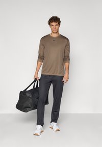 Brūns garo piedurkņu sporta krekls, melni sporta bikses, baltas kedas ar brūniem akcentiem un melns sporta soma. Gluda tekstūra.